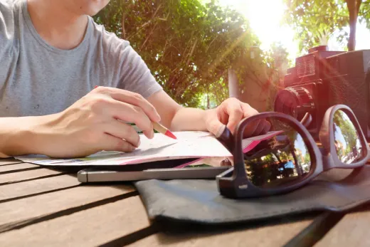 A person marking a route on a paper map at a wooden table
