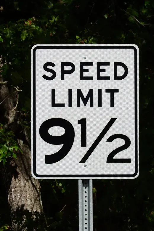 A white speed limit sign reading 9 and a half in front of dark trees