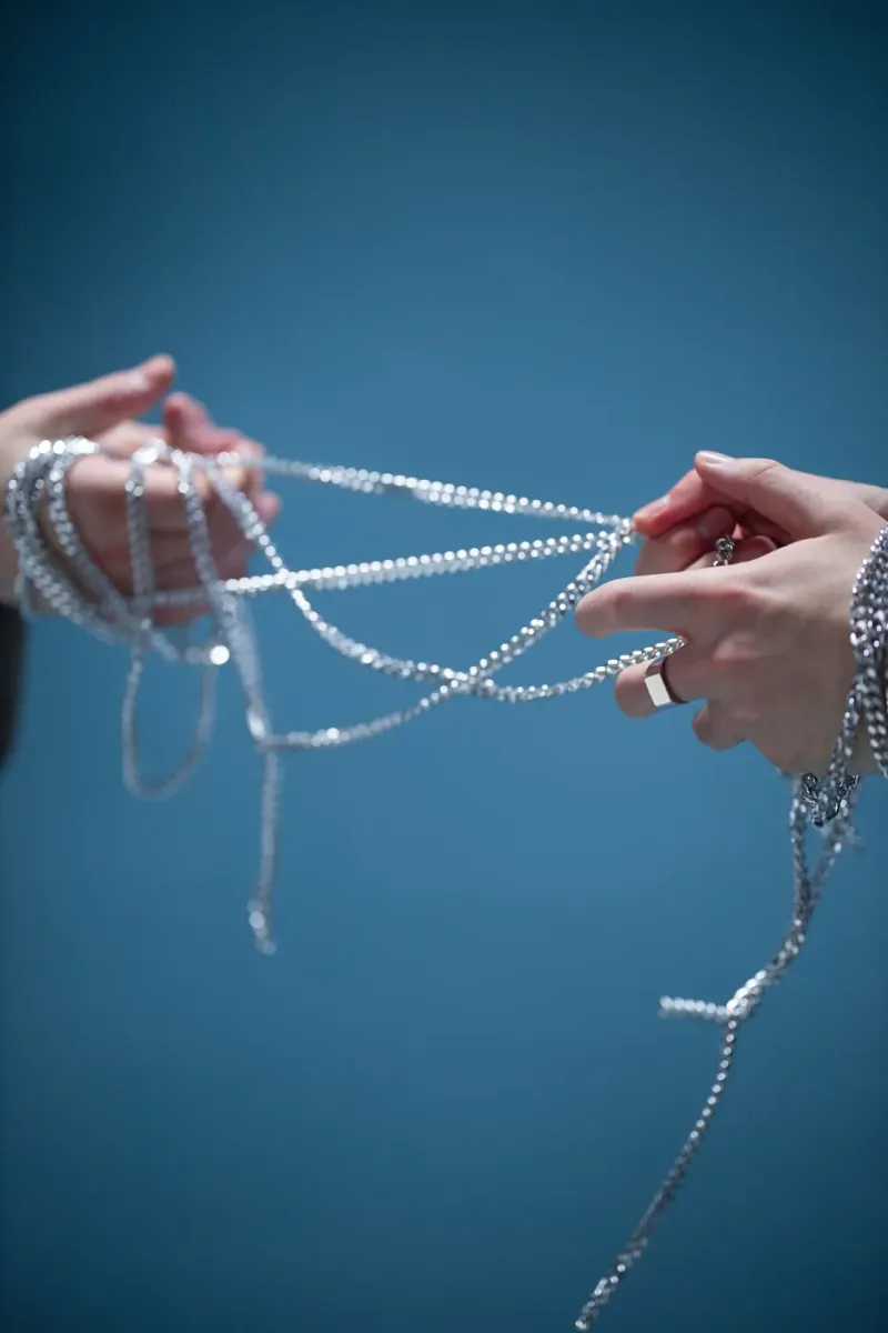 Hands untangling a long silver chain, standing for tangled dependency versions