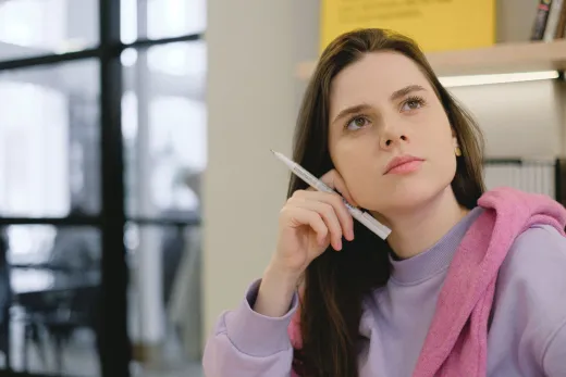 A woman holding a pen to her chin and looking up thoughtfully