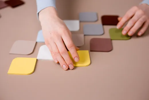 Hands fitting colourful flat tiles together on a pink surface