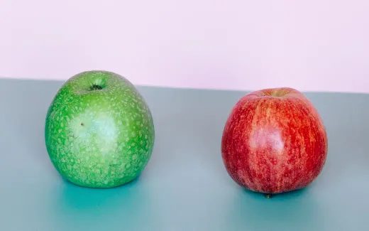 A green apple and a red apple side by side on a teal surface
